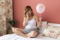 A smiling pregnant woman sitting in bed with pink balloon Ã¢â¬ÅitÃ¢â¬â¢s a girlÃ¢â¬Â talking over smart phone Royalty Free Stock Photo